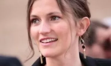 Person with brown hair smiling, wearing black earrings.